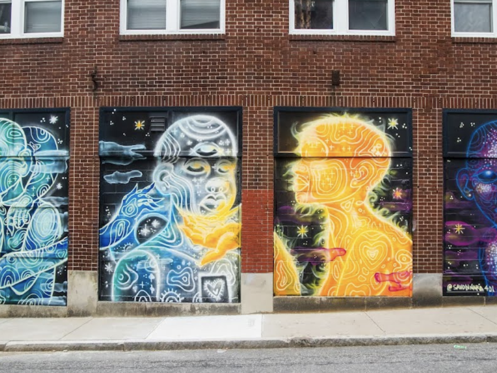 Four panel mural of figures interacting on a large wall. Sun, moon, universe and earth as embodied beings. Art, mural, caring, love, interconnectivity, connection. joy, dialogue, inclusion, The Avenue Concept